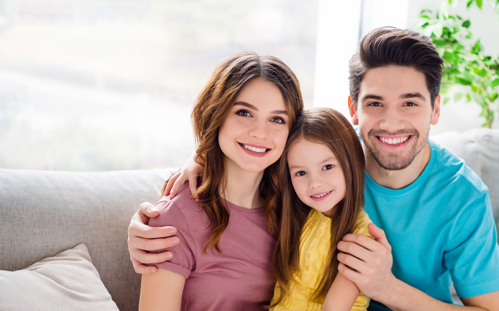 A family of three, a man, woman, and child, posing together for a photograph with smiles on their faces.