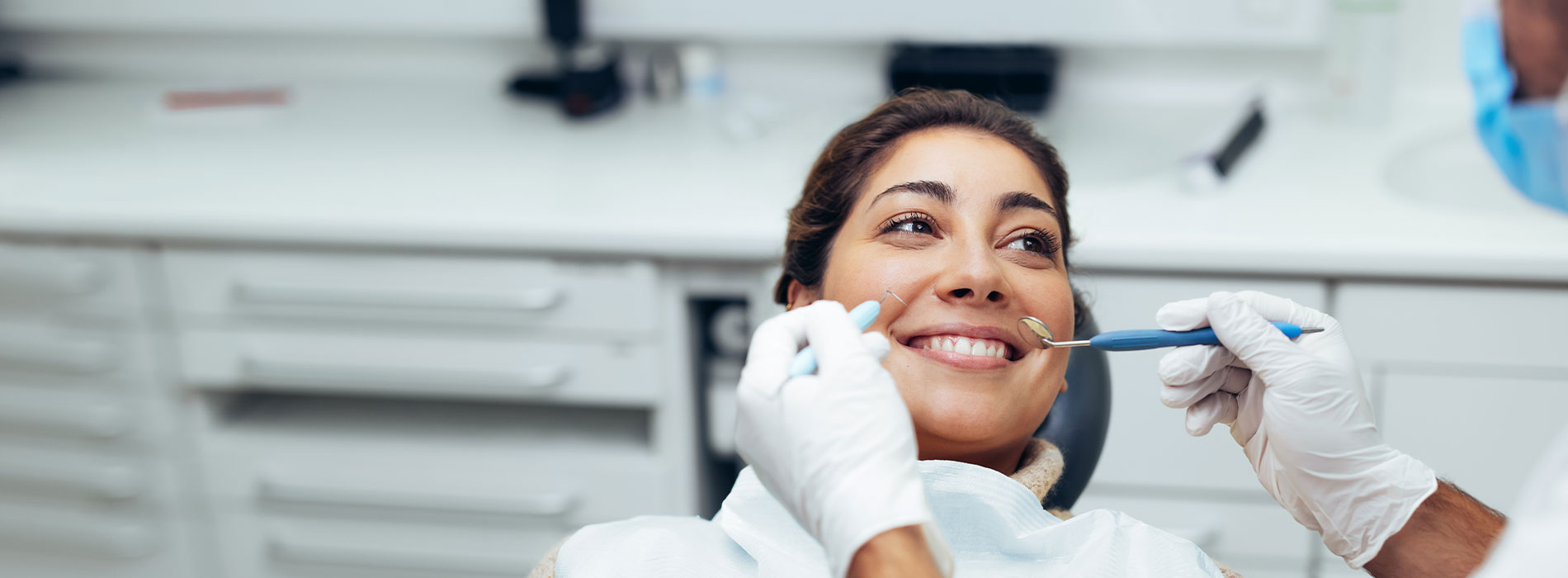 Dental hygienist performing a cleaning procedure with a patient in the background.