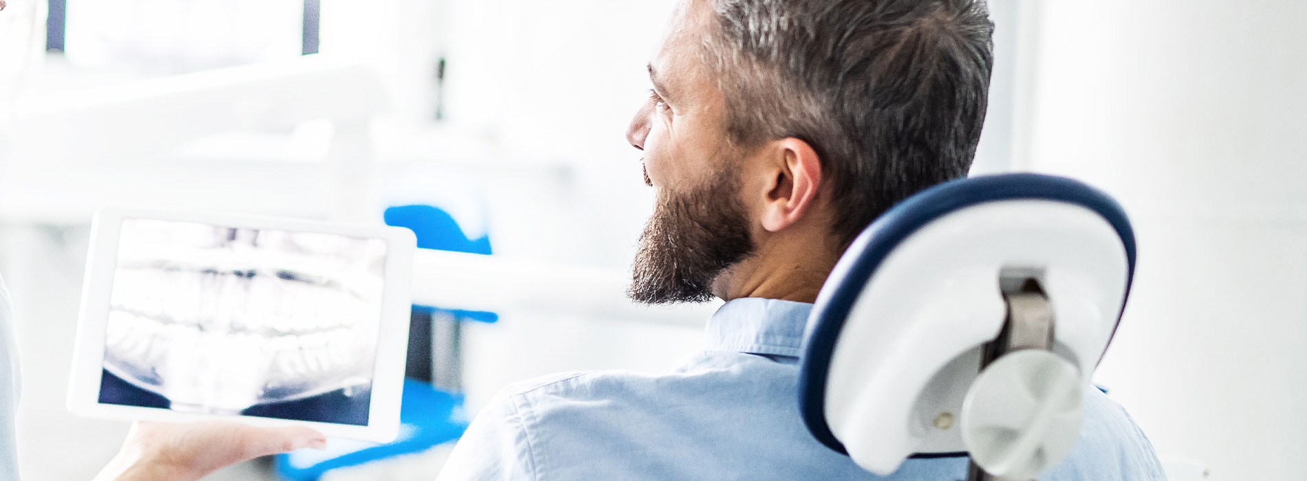 A man sitting in a dental chair, looking at a digital screen with a smile, set against a professional dental office backdrop.