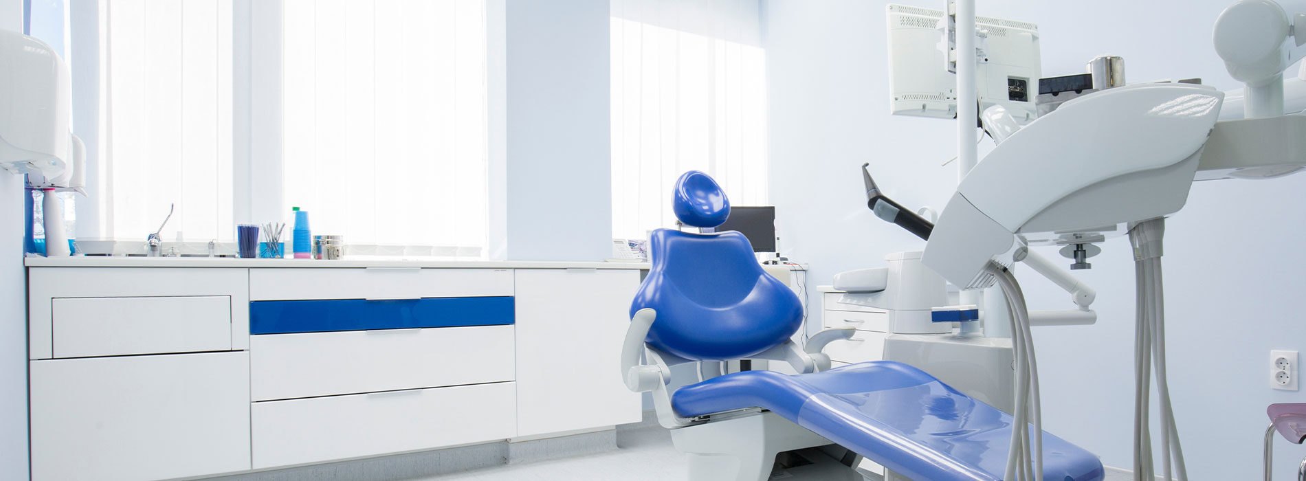 A modern dental office with a clean and sterile environment, featuring blue chairs, white walls, and professional equipment.