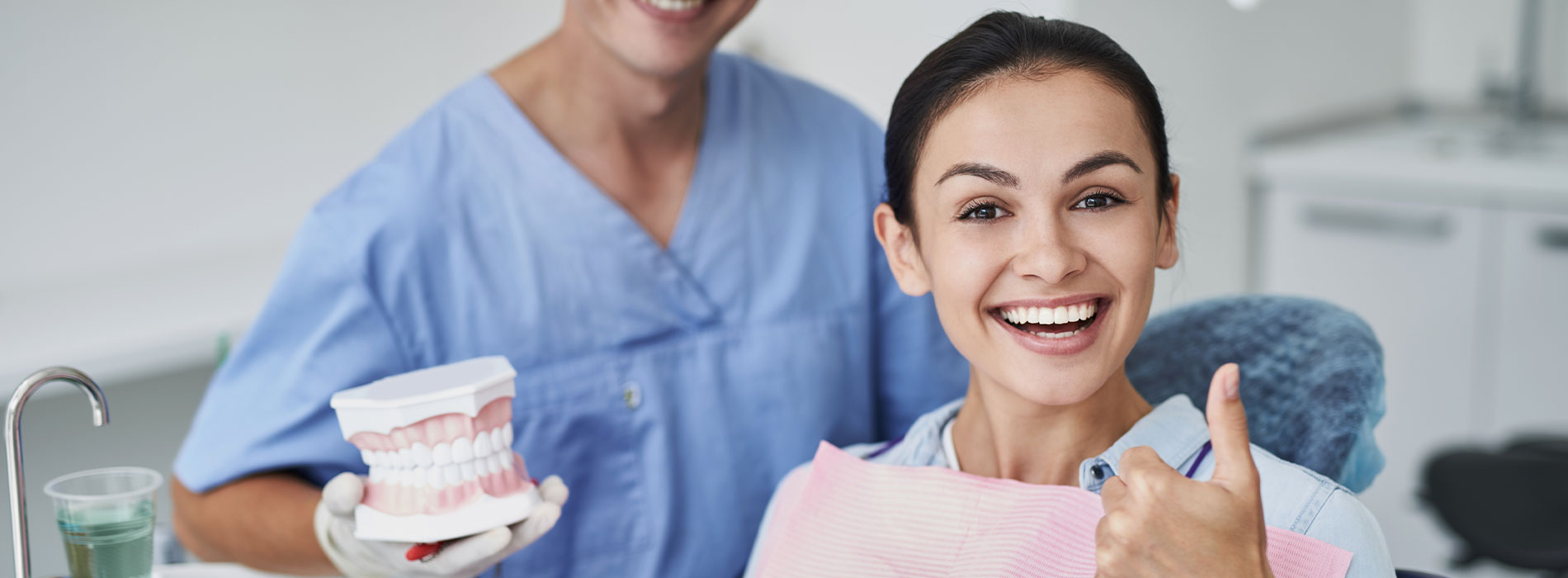 A dental professional and a patient are smiling in front of a dental chair.