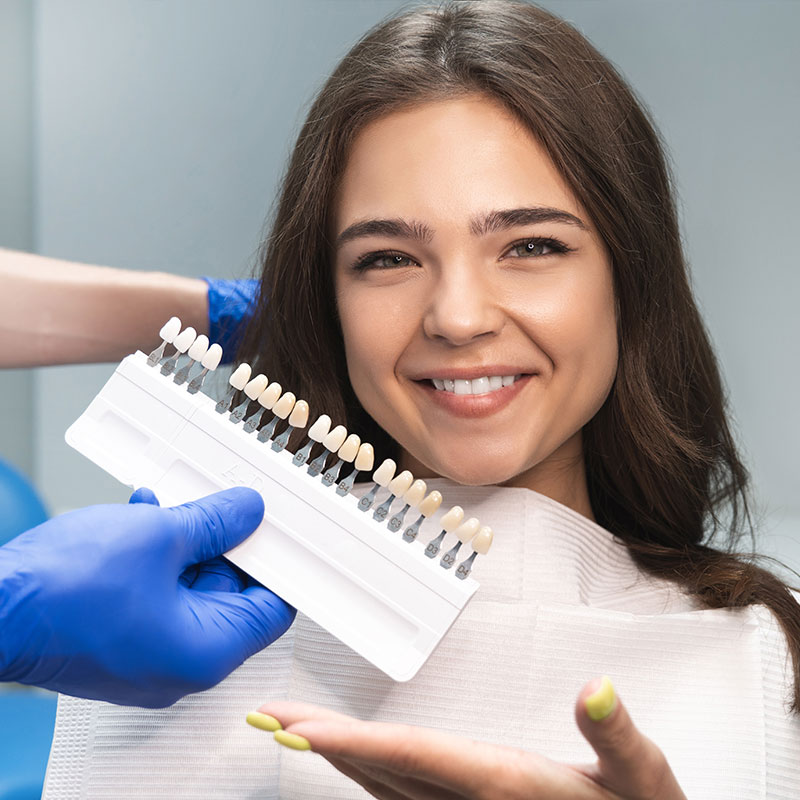 A woman with a bright smile is holding a tray of dental implants, showcasing the teeth-whitening process in a dental setting.