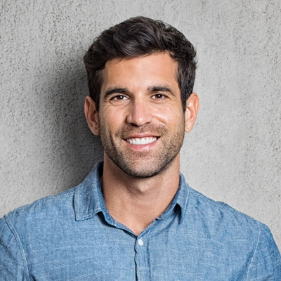 Smiling man with short hair, wearing a blue shirt and standing against a gray background.