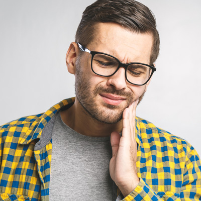 A man with a beard, wearing glasses and a yellow plaid shirt, holding his hand to his mouth in a thoughtful or concerned manner.