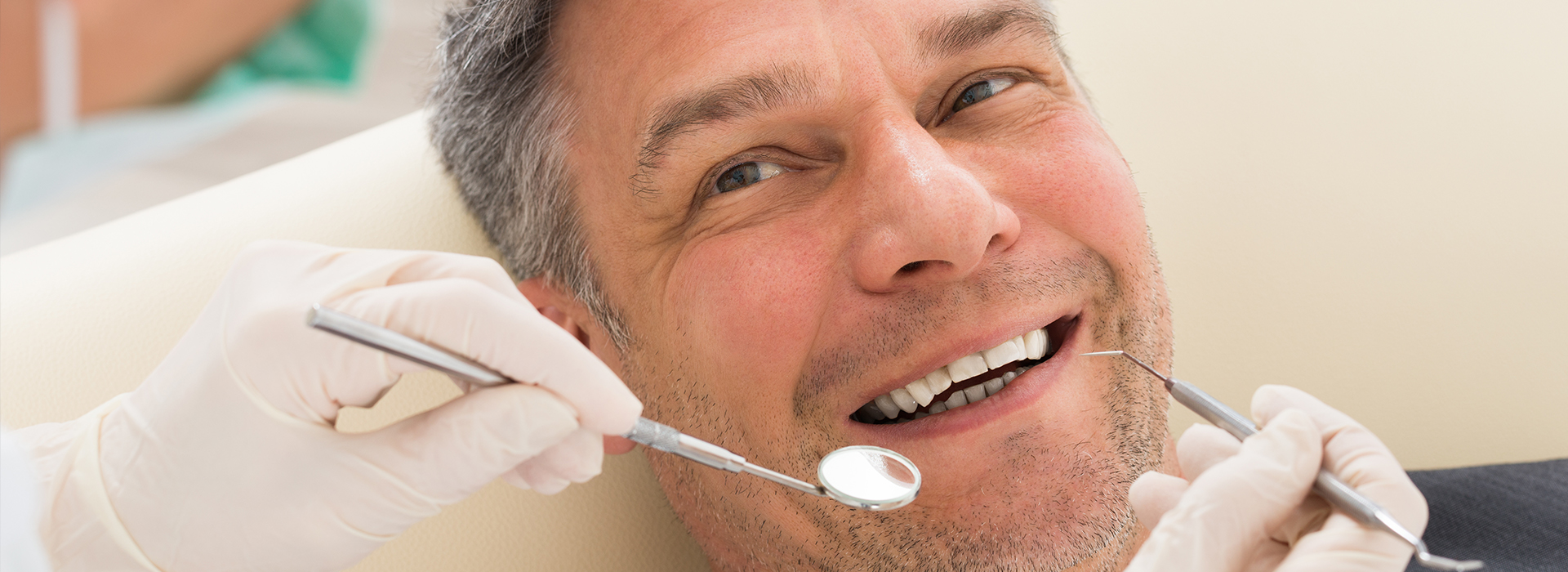 The image depicts a man in a dental chair, receiving dental treatment with a smiling expression.