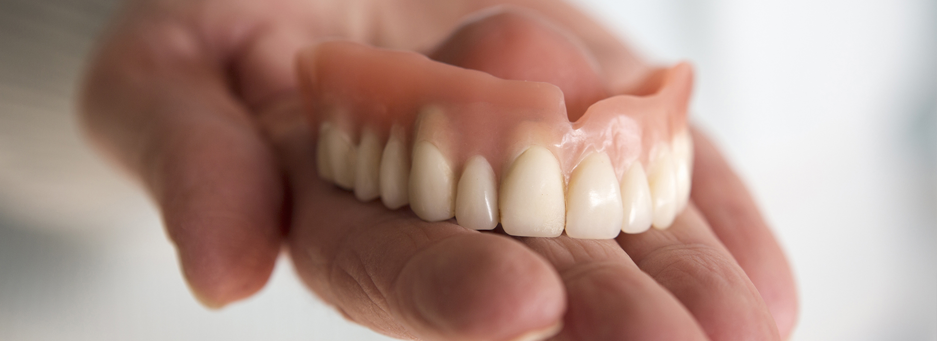 A person holding a set of dentures with teeth visible.