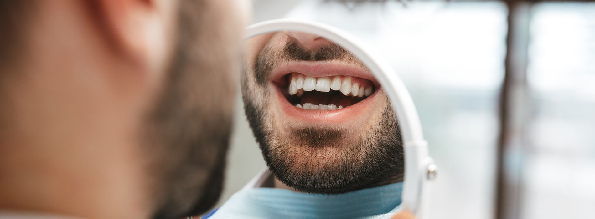 A man with a beard smiling at the camera, wearing a blue shirt and white headphones, in front of a blurred background.