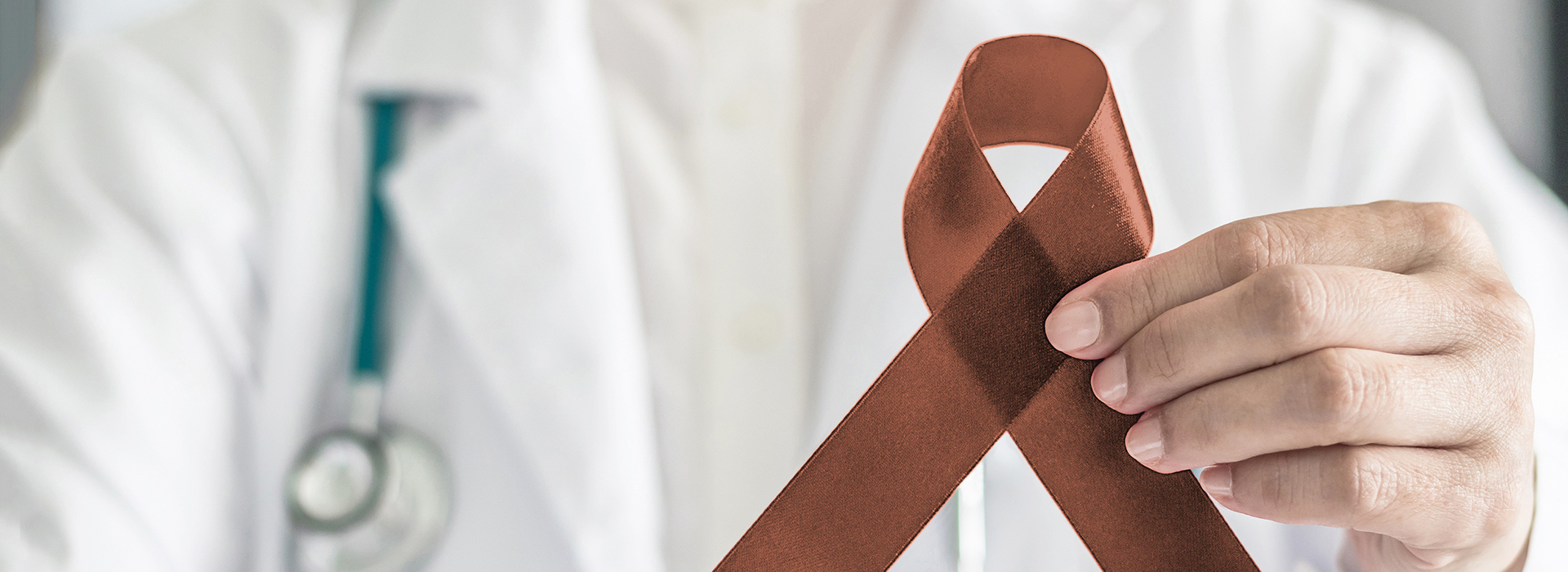 The image features a person holding up a ribbon with a symbol on it, which is commonly associated with awareness for cancer. The individual appears to be a healthcare professional, likely a doctor or nurse, given the stethoscope and medical attire in the background.