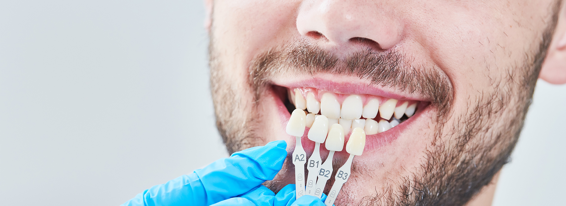 The image features a man with a toothy smile, wearing a blue surgical mask and holding a dental implant in his hand.