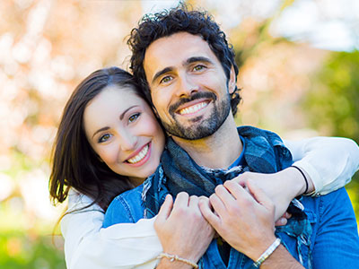 A man and a woman embracing, with the man wearing a bandana around his neck and both smiling at the camera.