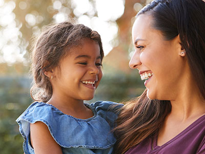 The image depicts a young girl and an adult woman, both smiling, with the child looking at the camera while standing close to the woman.