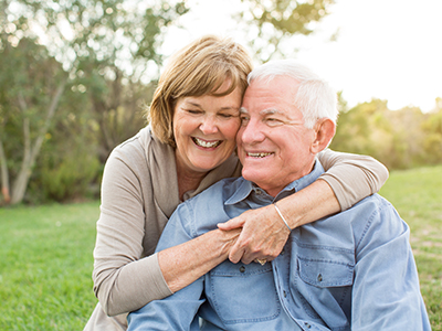 A man and a woman, both smiling, embrace each other in an outdoor setting.