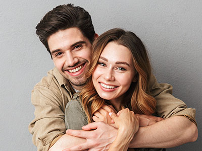 A man and a woman smiling and hugging, with the man wearing a light brown shirt.