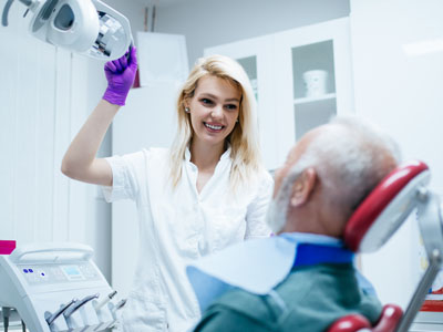 A dental professional, possibly a dentist or hygienist, is assisting an elderly patient with a dental examination in a modern dental office.