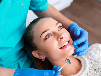 The image shows a dental professional performing a procedure on a patient s teeth, with the patient smiling and looking at the camera.