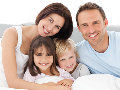 A family of five, including two adults and three children, posing together in a bedroom with a white bed.