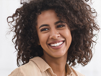 The image shows a person with curly hair and a broad smile, looking directly at the camera.